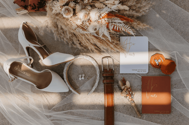 Some wedding accessories neatly arranged on a bed, including a dried flowers bridal bouquet and natural dried flowers boutonniere.