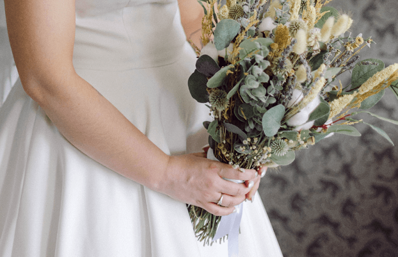 A bride holding a bouquet of wildflowers bound with a white ribbon.