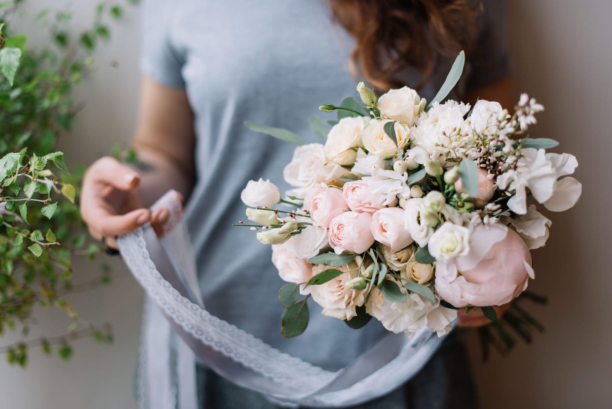 A woman adding white lace to a bouquet of flowers.