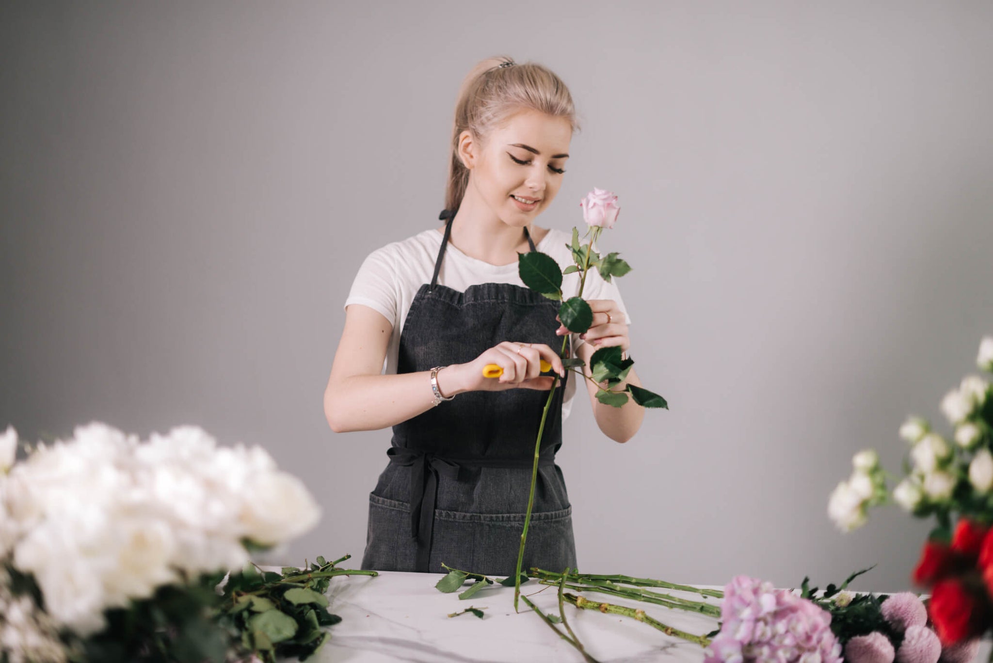 Woman removing the excess leaves from a long stem rose.