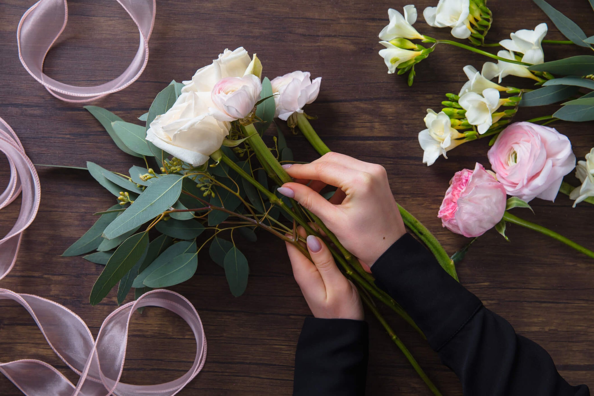 A woman arranging a mixture of rose sizes with some greenery on a wooden table.