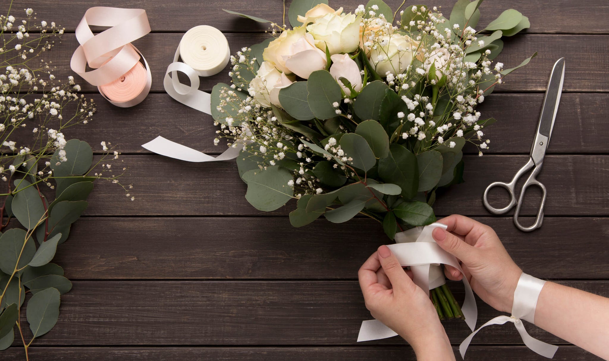 A person binding the stems of a bouquet with tape and ribbon.