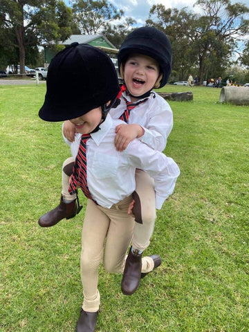 Two young girls at pony club, dressed up wearing black helmets, white shirts, red ties and cream jodhpurs.