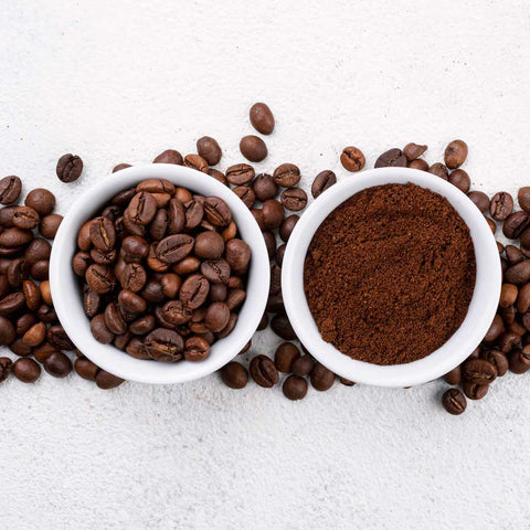 two cups, one with whole coffee beans and one with ground coffee on top of coffee beans on speckled background