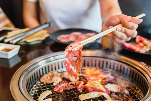 A woman with chopsticks grilling yakiniku meat.