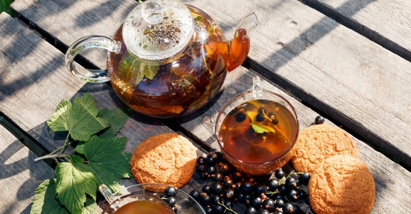 Black currant tea in a glass teapot with fresh currants and cookies on a wooden table