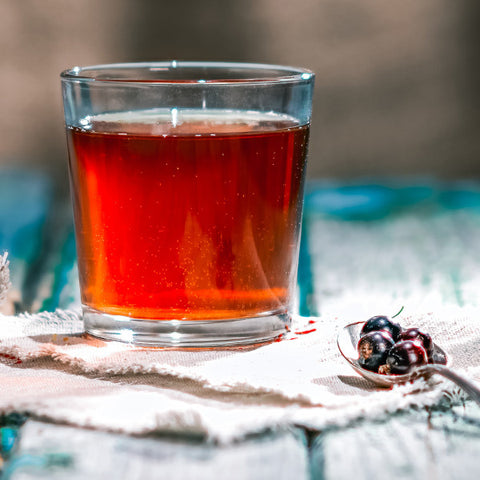 A glass of black currant tea witha spoon of fresh black currants to the side