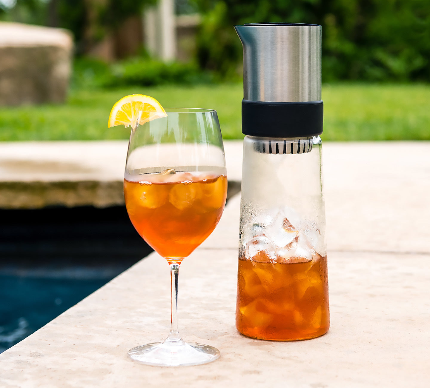 Blomus Tea Jay Iced Tea Maker and a glass of iced tea in a wine glass by a pool