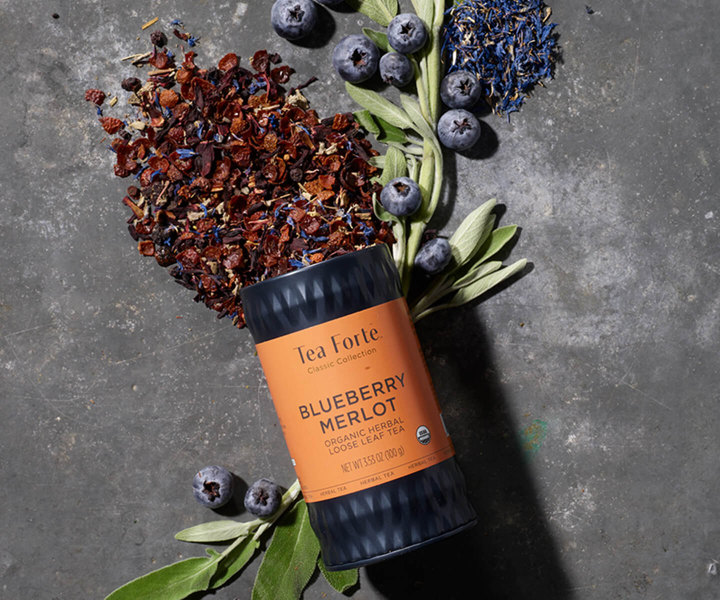 Blueberry Merlot Tea Canister laid back on dark stone with ingredients spilling out