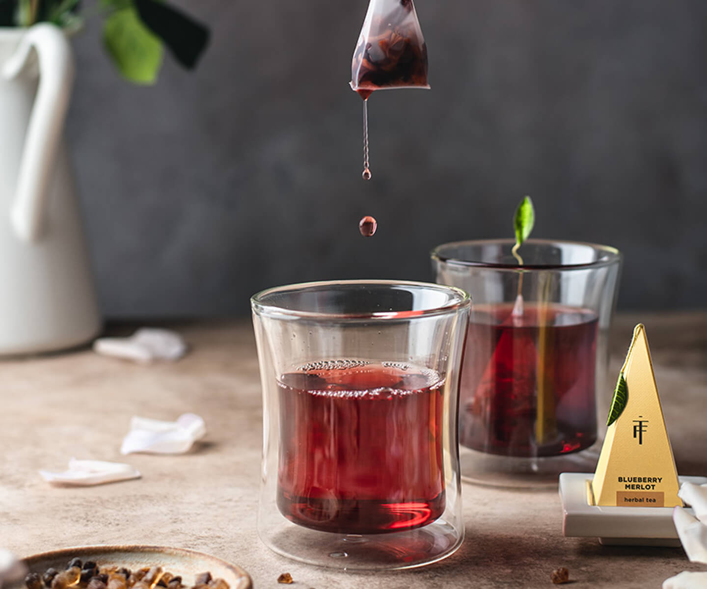 Blueberry Merlot Tea infuser being removed from a POOM glass, as the tea drips dramatically off the infuser from above.