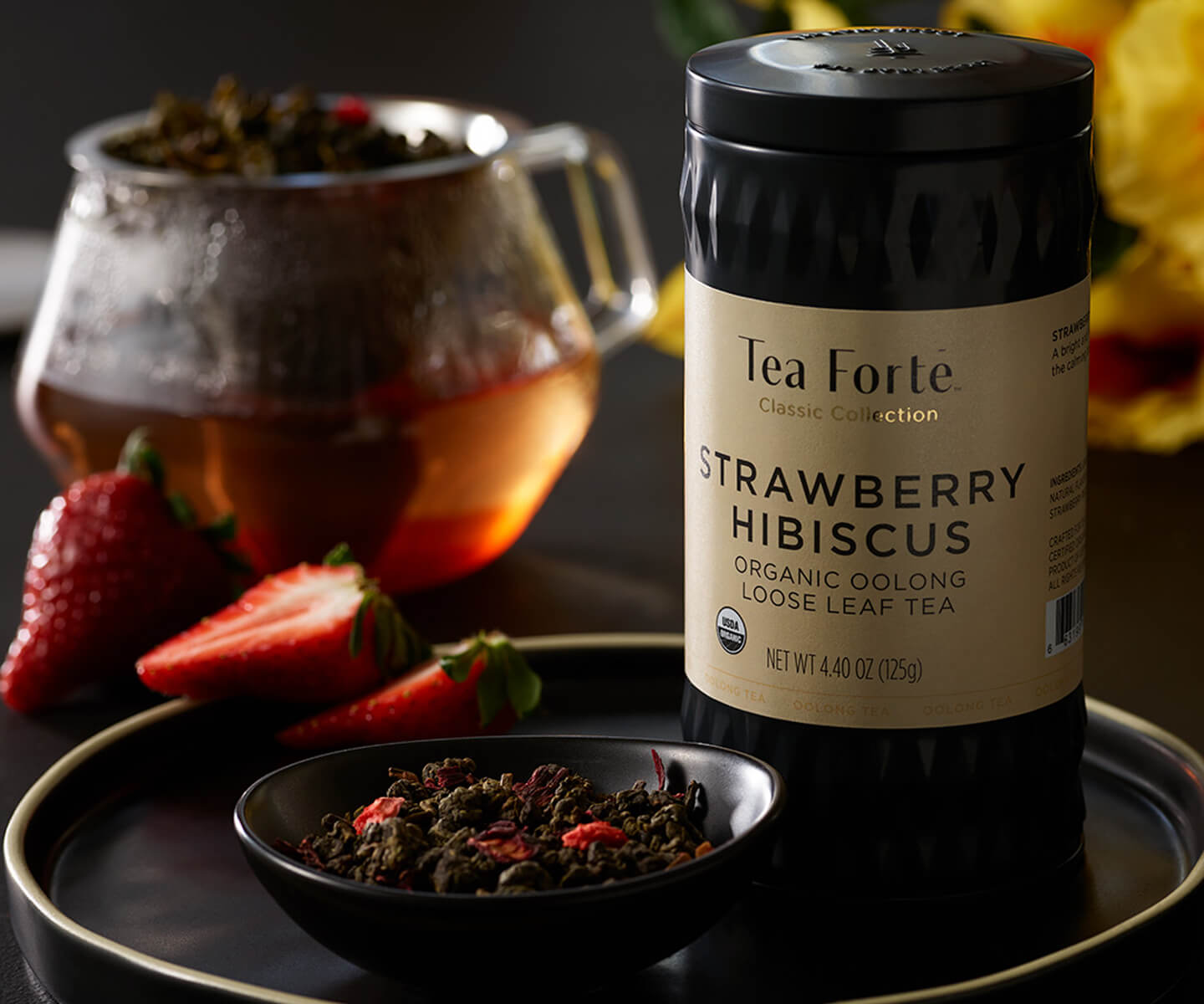 Loose leaf tea canister of Strawberry Hibiscus tea with strawberries and loose leaf tea in a bowl