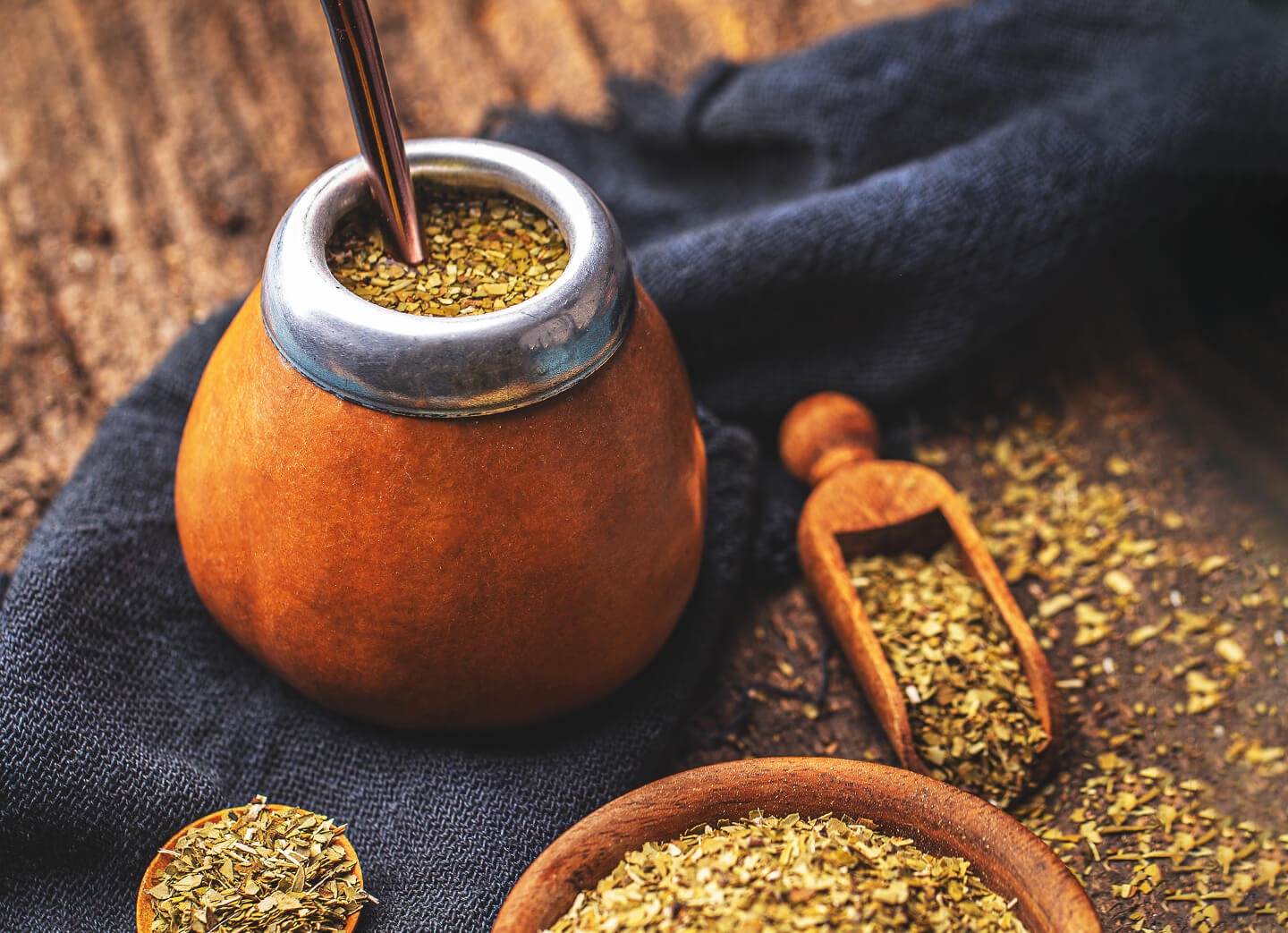 Maté tea in a gourd with bombilla and dried tea pile on a wooden tray