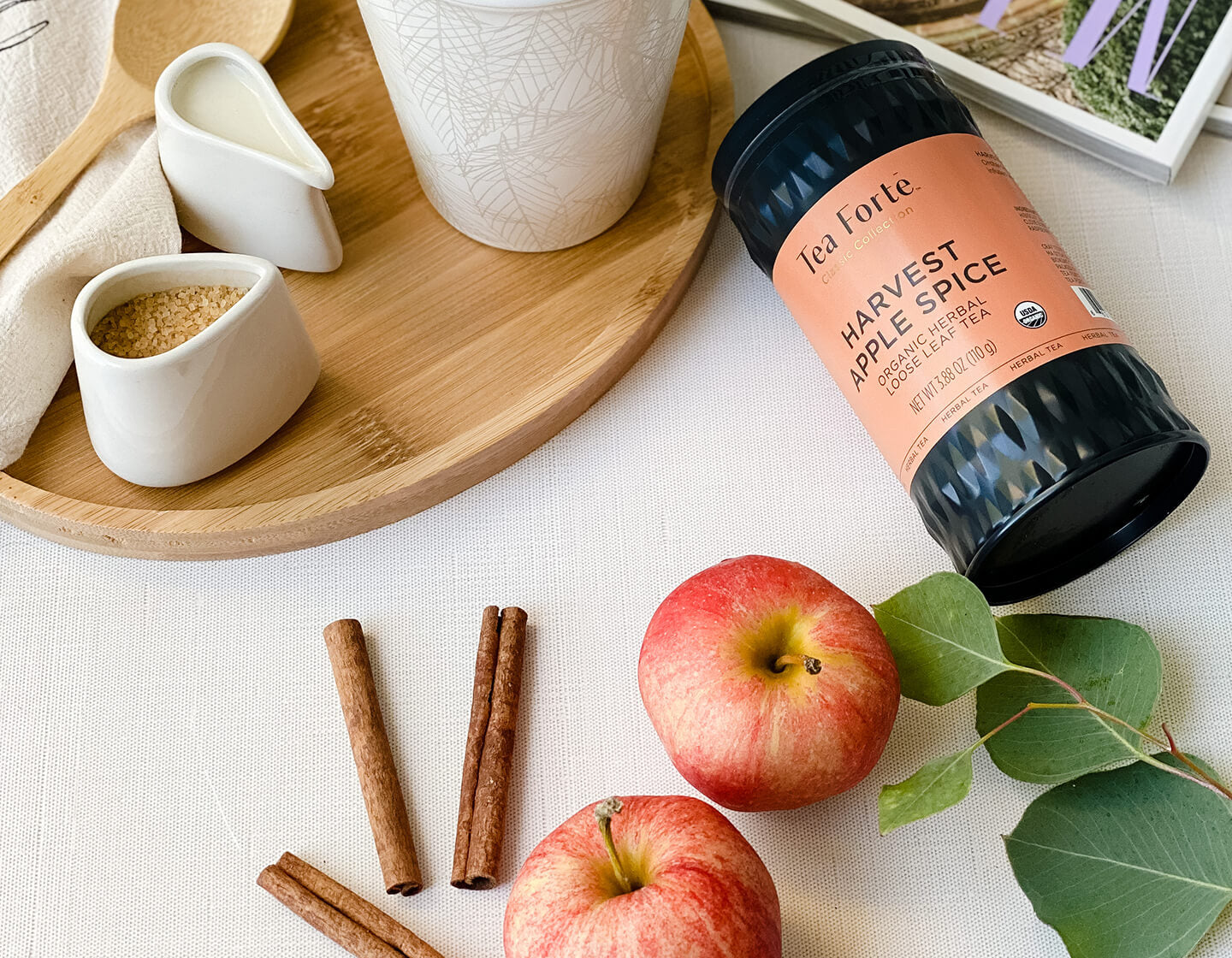 Harvest Apple Spice loose tea canister on a table with apples and cinnamon sticks.