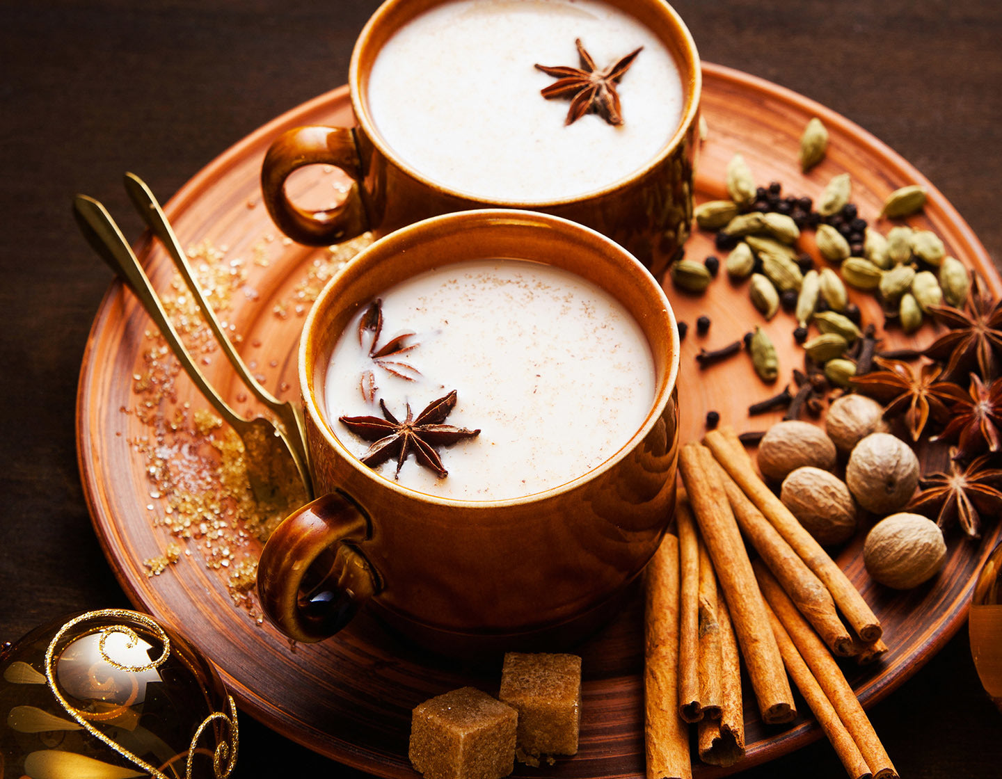 2 cups of Chai tea on a ceramic plate with milk foam topped with anise seed pods