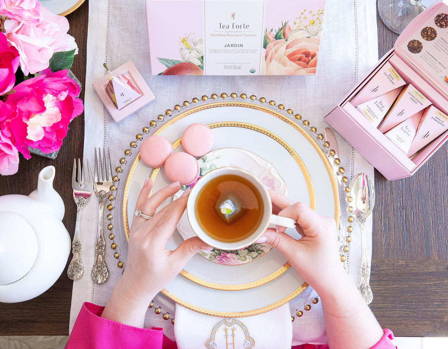 Holding a cup of Jardin tea on a table with pink cookies, gold-rimmed plates & pink napkins