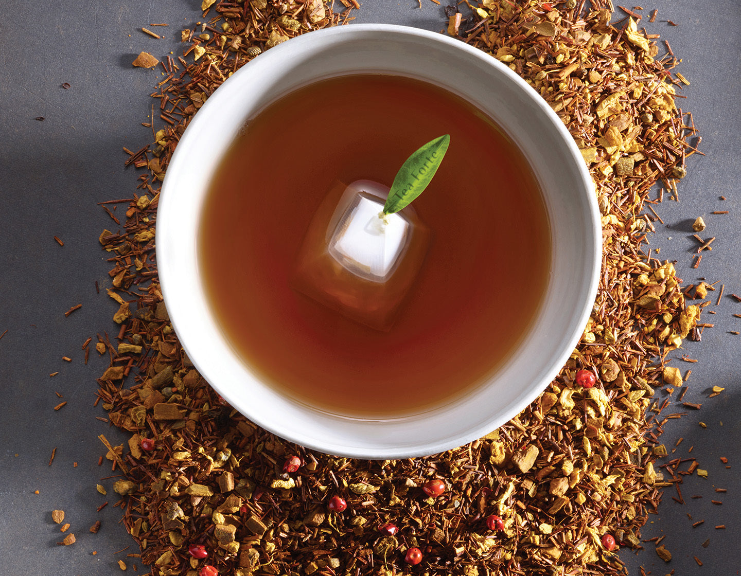 Cup of rooibos tea with a pyramid infuser inside, surrounded by loose leaf rooibos tea