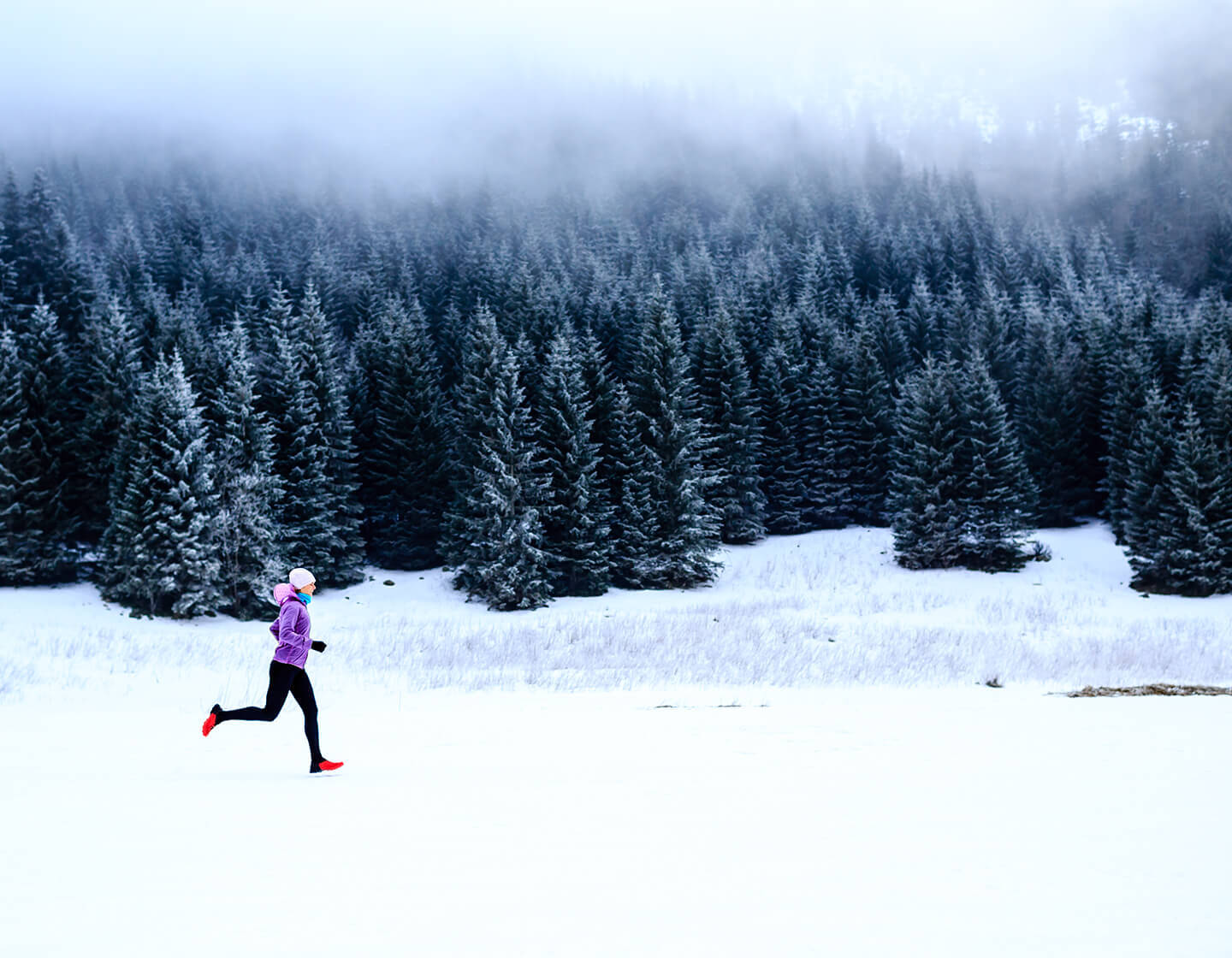 Woman trail running through a snowy landscape.