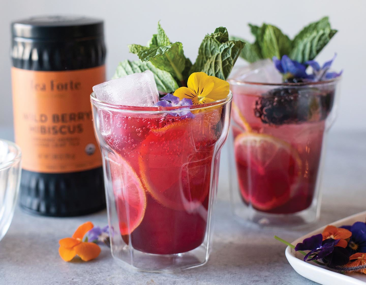 Wild Berry Hibiscus Spritzer decorated with violets and a loose tea canister in background