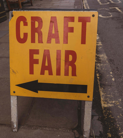 a yellow sandwich board style sign reads "Craft Fair" in red with a black arrow pointing left