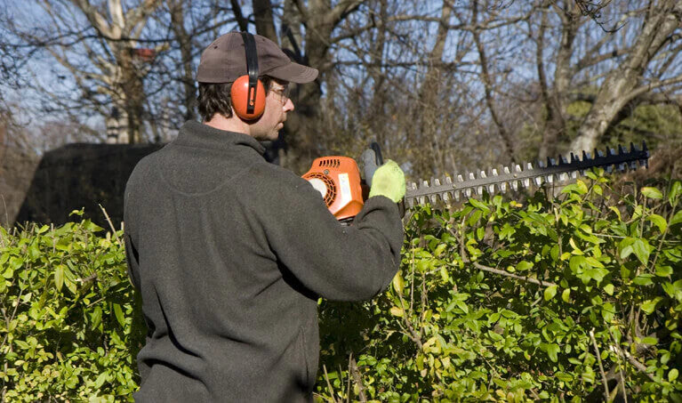 Man trimming bushes while wearing safety glasses