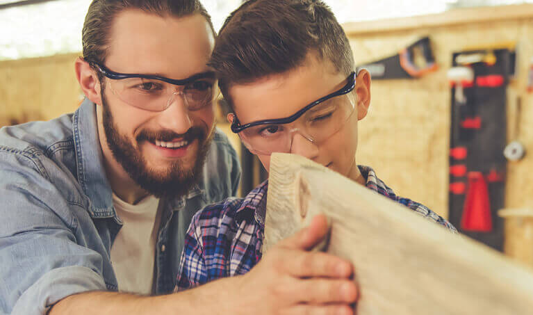 Father and son wear safety eyewear while woodworking.