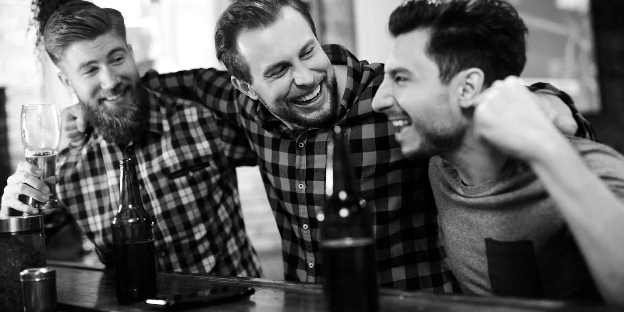 Three joyful men in a casual setting, laughing and enjoying a conversation over drinks, depicting the relaxed camaraderie that Core Benefits Toowoomba envisions for the future of men's massage.