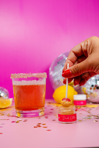 Woman dips lollipop into Drink Glitter container for a Disco Lemonade drink recipe
