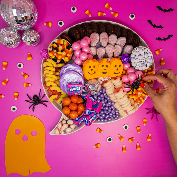 Woman places glitter spider prop on pink disco Halloween Candy Charcuterie Board
