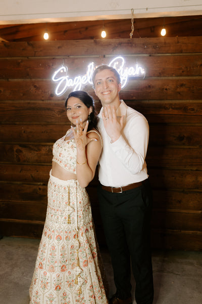 Couple shows off wedding rings in front of neon sign during wedding reception in Austin, TX