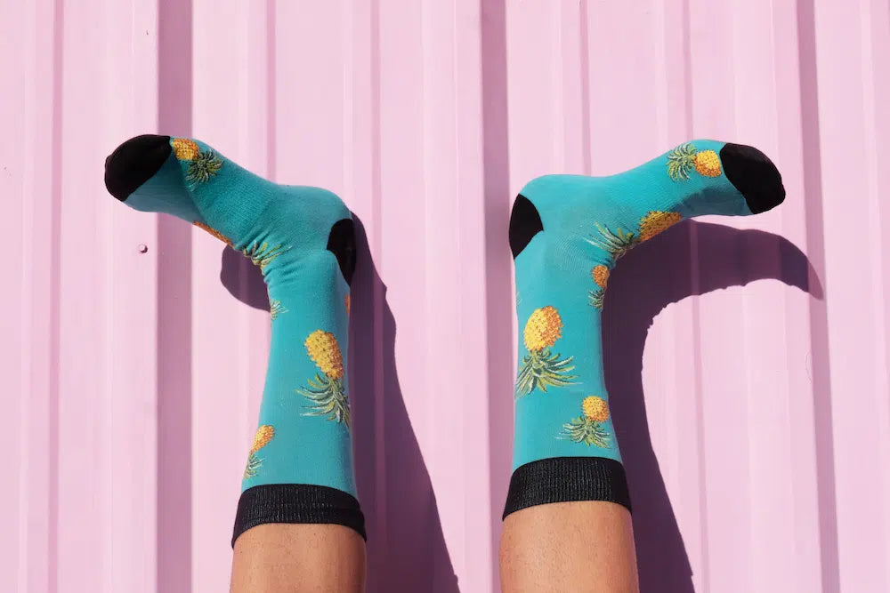 A person's legs crossed and raised against a pink wall, wearing bright blue socks with a pineapple pattern.