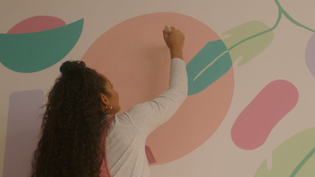 Woman with long dark curly hair painting a colourful mural with YesColours pastel paint colours