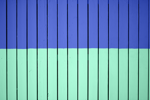 a closeup photo of a two-tone wooden floorboard where the top half is painted in a blue purple colour and the bottom half is painted in a bright mint green colour