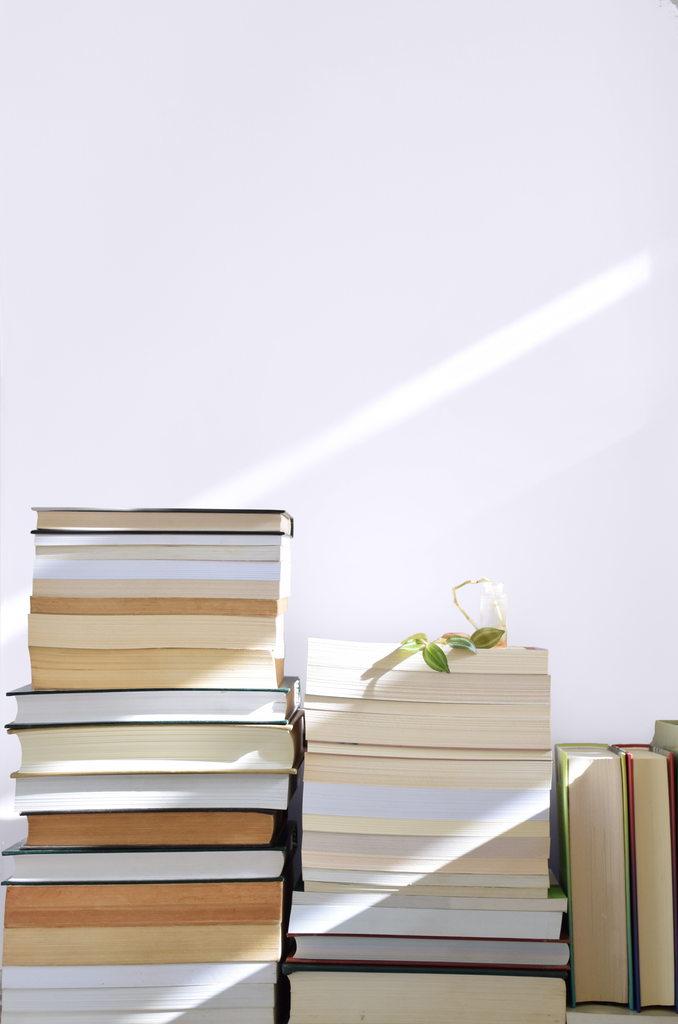 Vintage books stacked on top of each other in three columns, photographed in front of a light lilac wall
