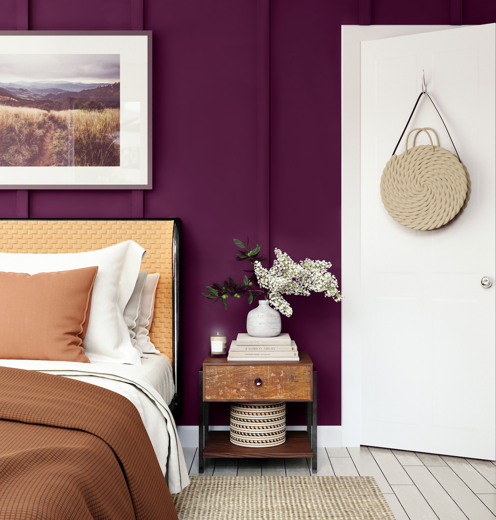 Bedroom shot with a white wall, rattan bed and bedside table, landscape nature photograph and a wall painted in a dark purple Pantone Colour of the Year 2023 Viva Magenta