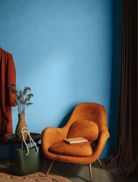 Burnt orange vintage mid-century chair, placednext to earthy-coloured vintage clothes and home accessories and photographed in front of a muted blue wall