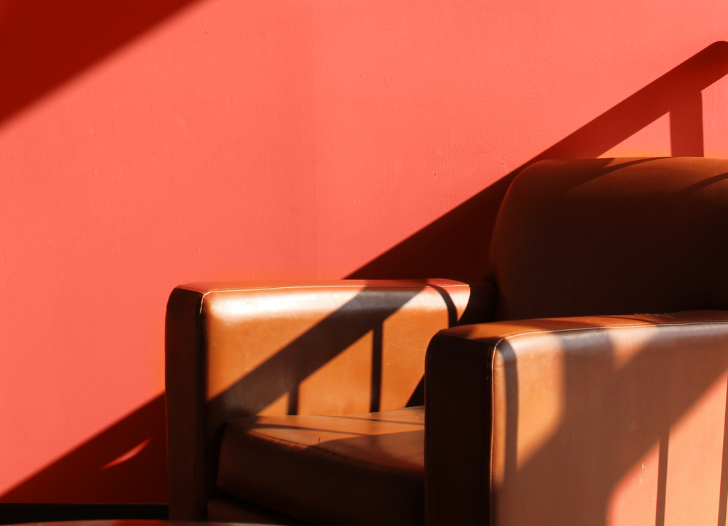 Sun light reflecting on a wall painted with YesColours Joyful Orange paint colour, with a tan leather chair photographed in front of it