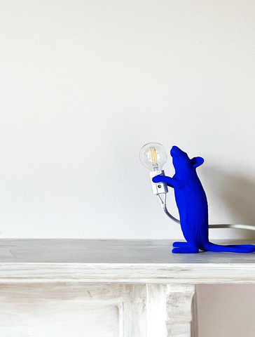 photo of a fireplace surrounding in white moving to a white-painted wall with an ultramarine blue-painted mouse figurine holding a circle light bulb