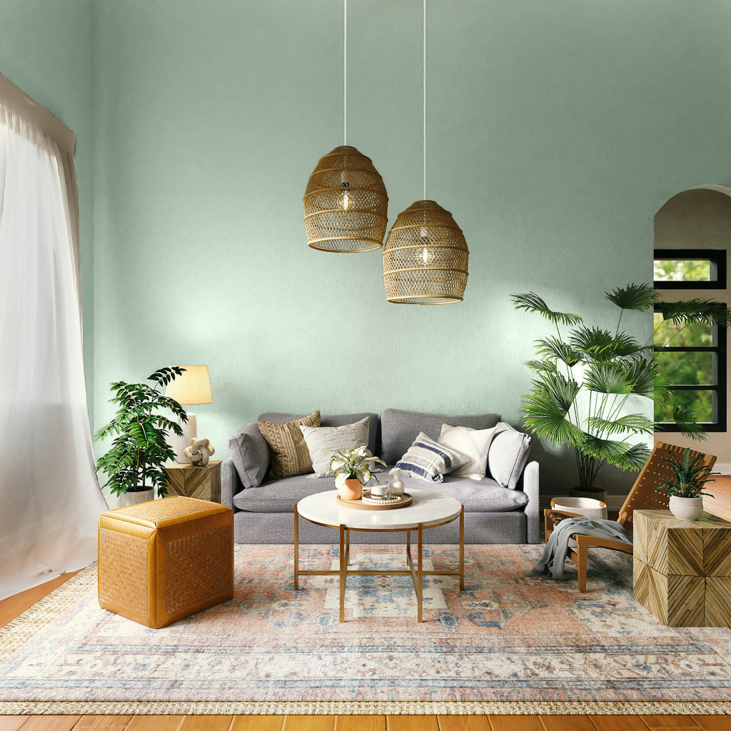 photo of a spacious living room with light green painted main wall, surrounded by a neutral-coloured sofa, a wooden table, rustic orange ottoman and rattan accessories, all placed on a vintage orange rug