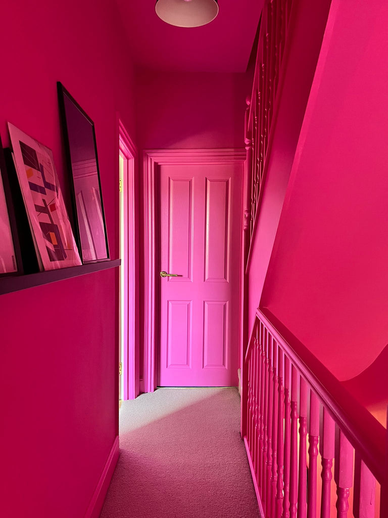 A narrow hallway with a central door and stairwell on the right, all colour drenched and painted entirely in YesColours Passionate Pink hot pink paint colour