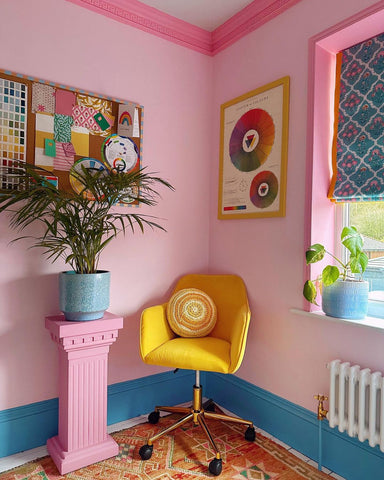 Home office corner with pink walls, blue skirting boards, dark pink alcoves, colourful posters and a yellow rotating office chair placed in the corner