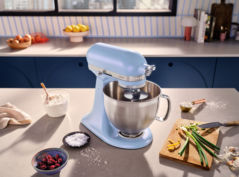 close up of a KitchenAid stand mixer in iridescent blue and lilac colour, placed on a kitchen worktop and surrounded by food