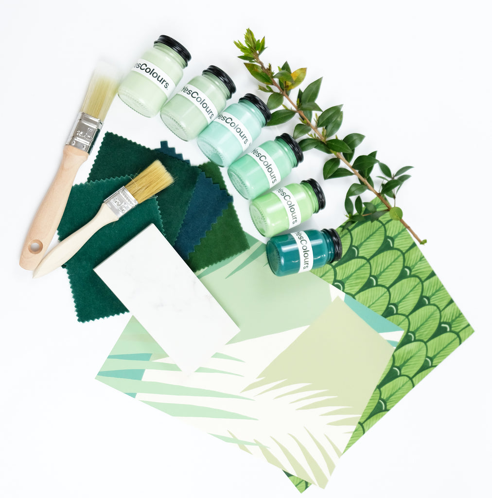 Flat lay photo of YesColours green paint samples next to fabric and wallpaper samples, paint brushes and a green tree branch