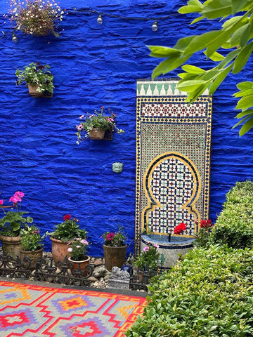 Marrakech-inspired garden with multicoloured rug on the floor, Electric Blue painted concrete wall and a Middle-Instern-style fountain placed on the wall and surrounded by hanging plants