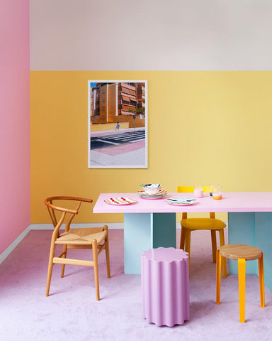 colourful dining room with a bright yellow and white wall, pink and aqua coloured geometrical table, purple carpet and an architecture photography print hanging on the wall