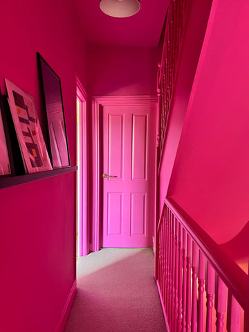 photograph with a narrow hallway, all painted in a hot pink colour including door, ceiling, walls and banisters