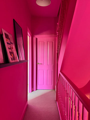 A small narrow hallway with light beige fitted carpet and stairwell on the right side, all painted in a hot pink colour