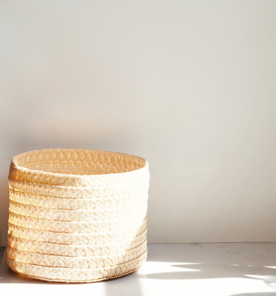 a pale yellow natural coloured woven basket photographed in front of a white painted wall