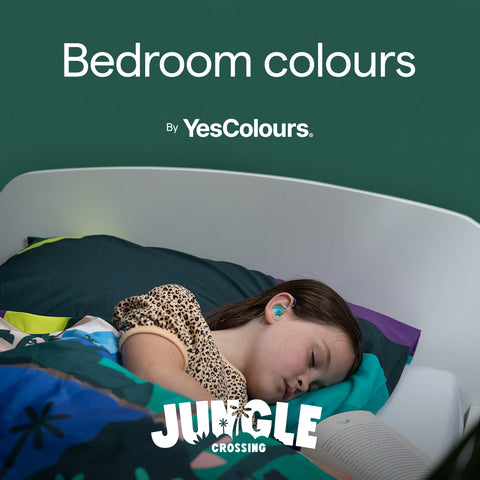 photo of a sleeping kid in a colourful dark green bedding, photographed in a bed positioned in front of a dark green wall