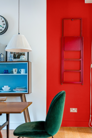 A split wall design with white on the left and red on the right, photographed behind a pastel blue vintage Mid-Century sideboard, a wooden desk and a velvet green desk chair