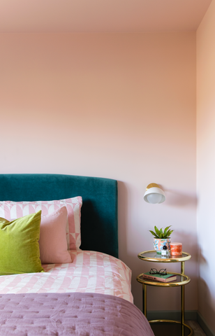 close up of a bedroom with peach coloured walls, dark teal headboard and bedding and cushions in pastel pink, peach and green colours